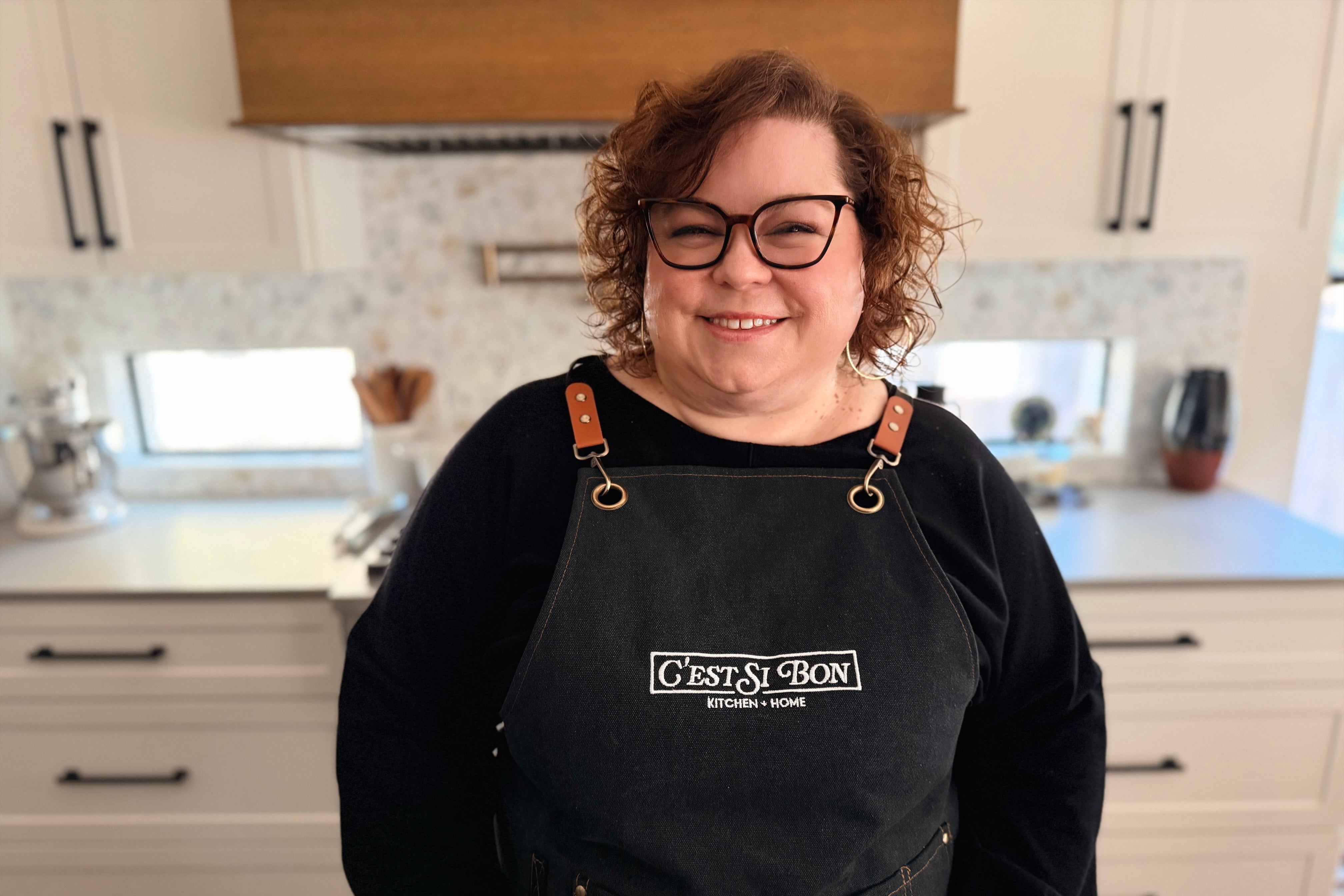 Ali Rastiello wearing a black apron with 'C'est Si Bon' logo in a kitchen setting