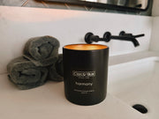 C'est Si Bon-branded black ceramic jar candle in the Harmony scent on a bathroom counter.
